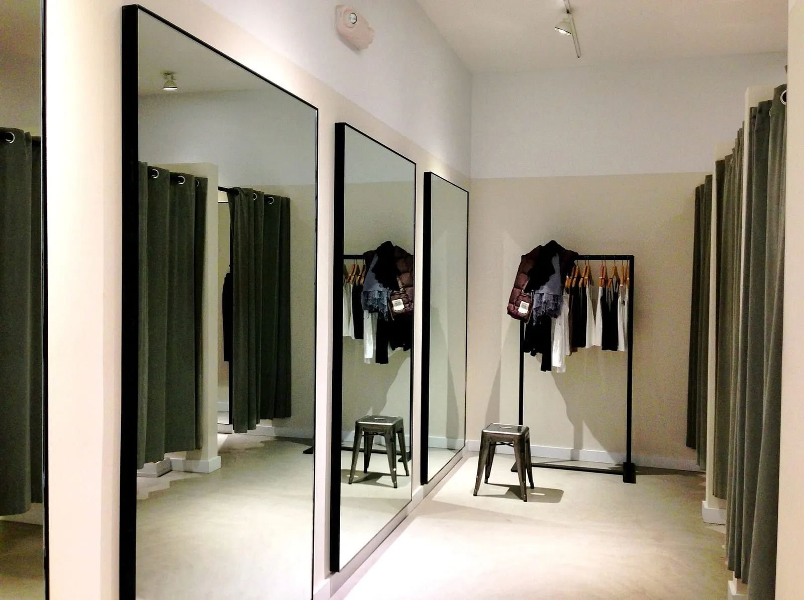 A bright fitting room with full-length mirrors, curtained cubicles and a rail of garments on hangers