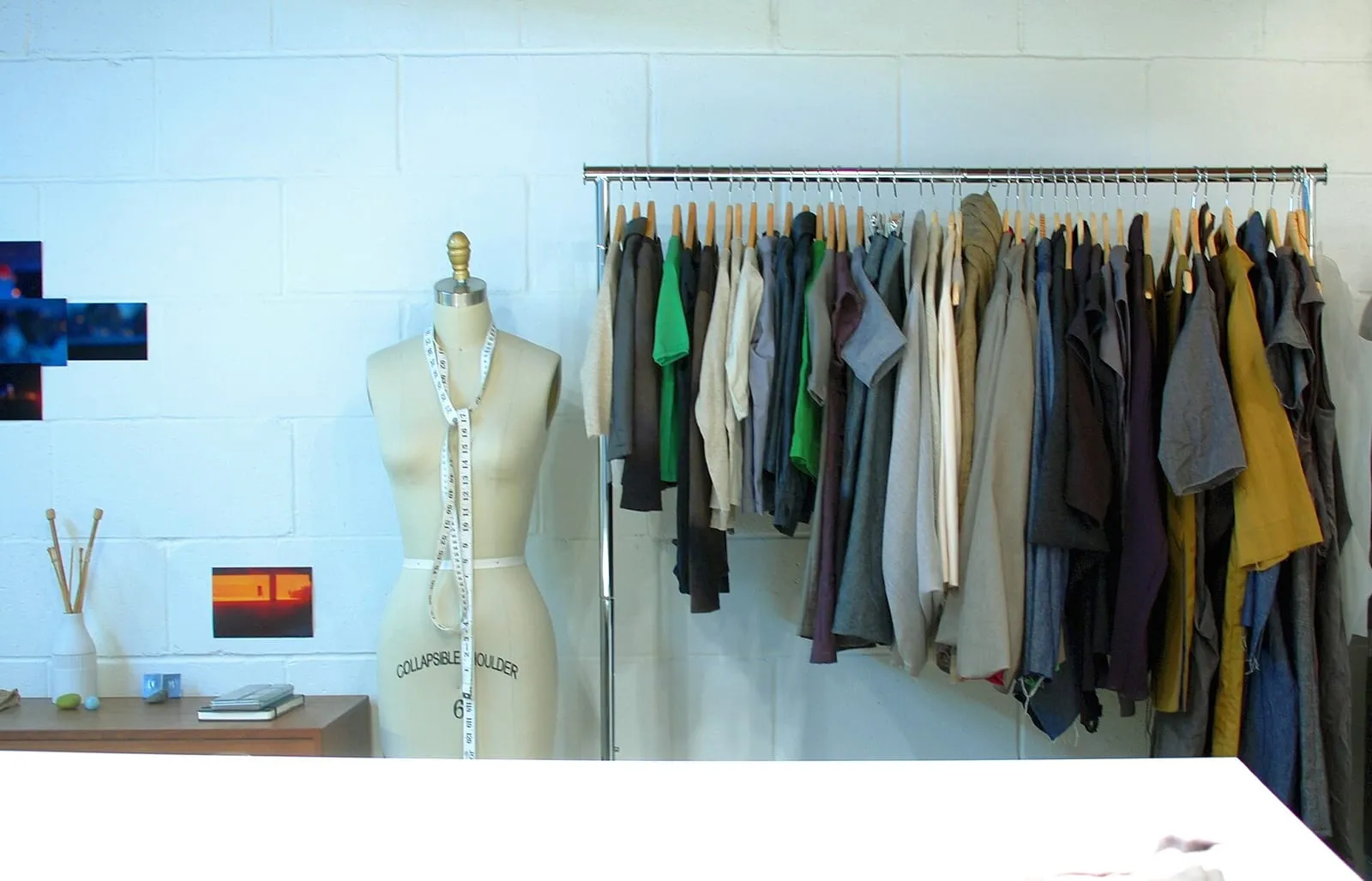 A sewing studio: a dress form with a tape measure around it beside a rail of finished garments